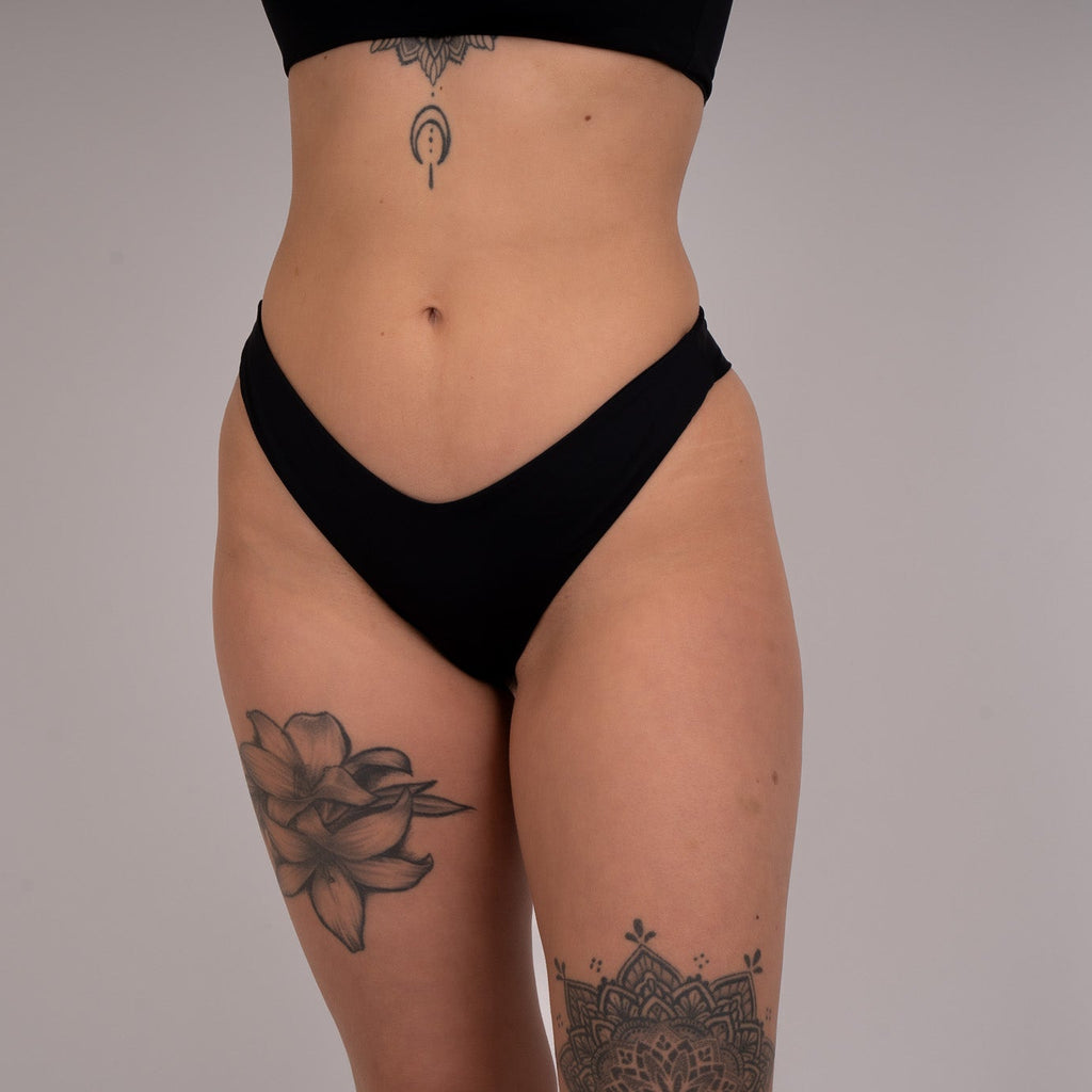 Person wearing a black thong against a plain background