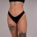Person wearing a black thong against a plain background